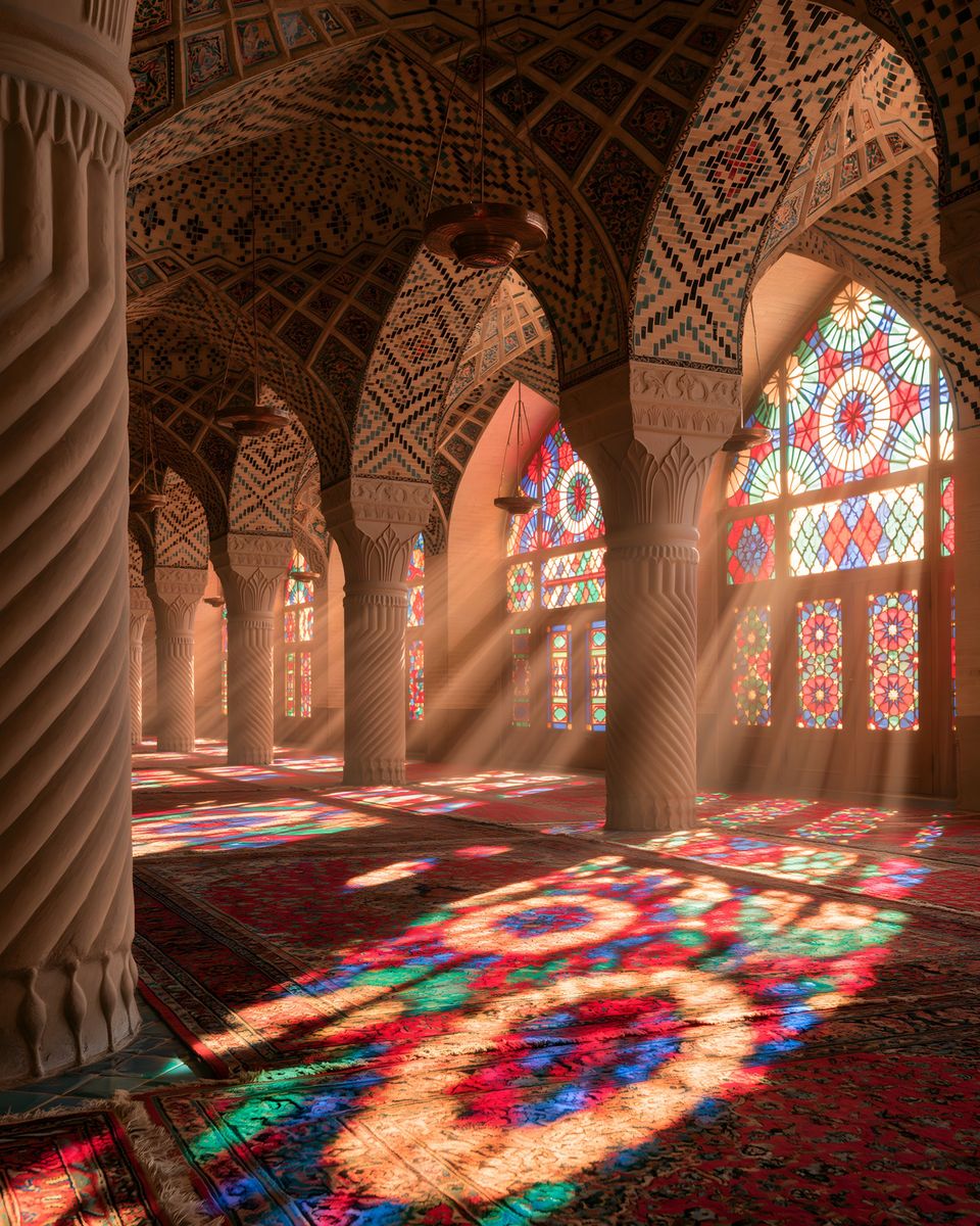 Morning light through stained glass scattering colour across the carpets and carved columns of the Nasir al-Mulk Mosque.